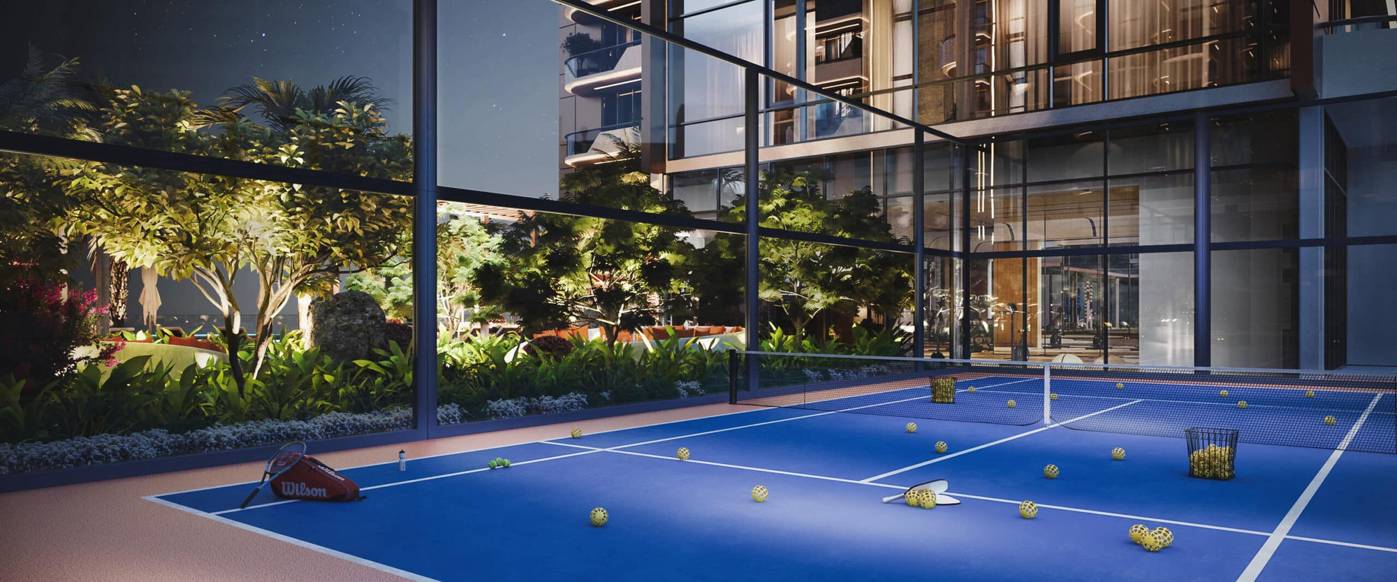מגרש טניס מקורה ומודרני עם קירות זכוכית ב”The Orchard Place” בשעות הלילה, עם כדורי טניס ומחבט על משטח המגרש הכחול; בחוץ נראים צמחייה עבותה ובניין מואר. מגרש טניס מקורה ומודרני עם קירות זכוכית ב"The Orchard Place" בשעות הלילה, עם כדורי טניס ומחבט על משטח המגרש הכחול; בחוץ נראים צמחייה עבותה ובניין מואר.
