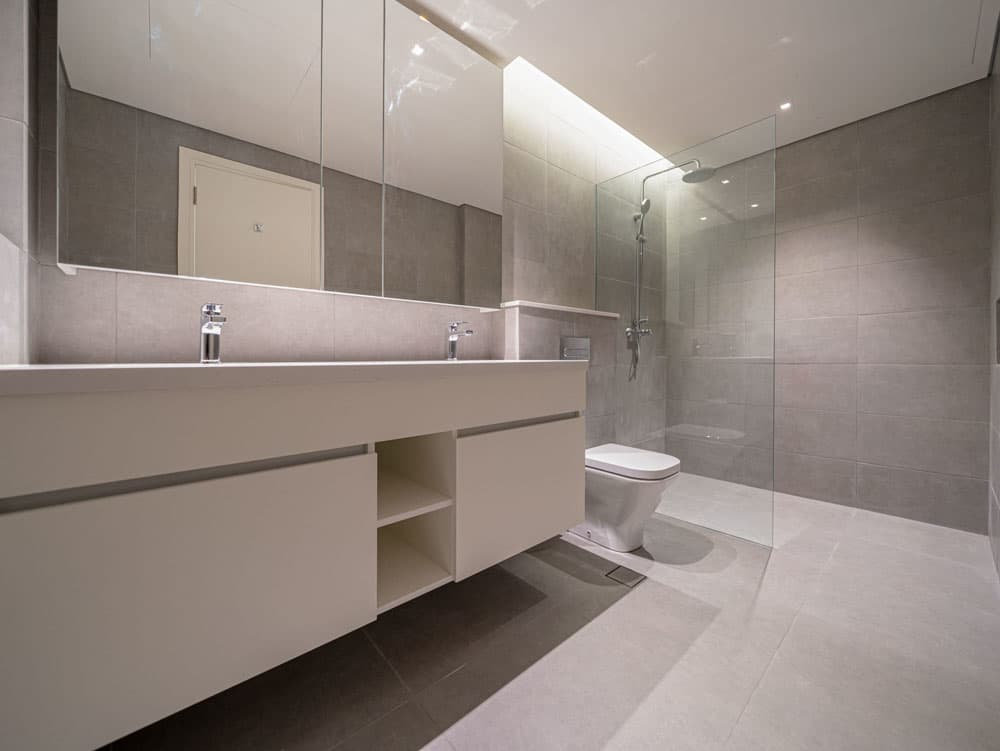 חדר הרחצה המודרני ב-Ahad Residences כולל שידת רחצה גדולה עם כיורים כפולים, מראה רחבה ומקלחת מוקפת זכוכית. אריחים בצבע אפור בהיר מכסים את הרצפות והקירות, ויוצרים חלל מואר ומינימליסטי. חדר הרחצה המודרני ב-Ahad Residences כולל שידת רחצה גדולה עם כיורים כפולים, מראה רחבה ומקלחת מוקפת זכוכית. אריחים בצבע אפור בהיר מכסים את הרצפות והקירות, ויוצרים חלל מואר ומינימליסטי.