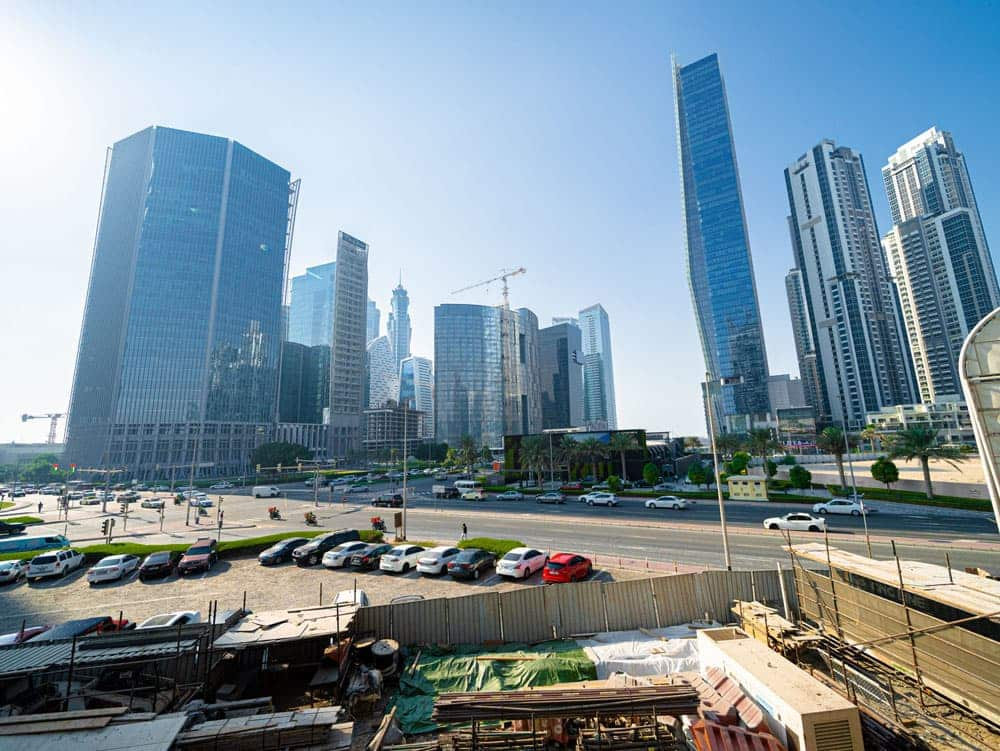 נוף עירוני מודרני עם גורדי שחקים גבוהים מזכוכית תחת שמיים כחולים וצלולים. רחוב הומה אדם, שבו מכוניות חונות ונוסעות, עובר מול הבניינים. ניתן לראות חומרי בנייה ליד דירות היוקרה של “אהד רזידנס” בדובאי. נוף עירוני מודרני עם גורדי שחקים גבוהים מזכוכית תחת שמיים כחולים וצלולים. רחוב הומה אדם, שבו מכוניות חונות ונוסעות, עובר מול הבניינים. ניתן לראות חומרי בנייה ליד דירות היוקרה של "אהד רזידנס" בדובאי.