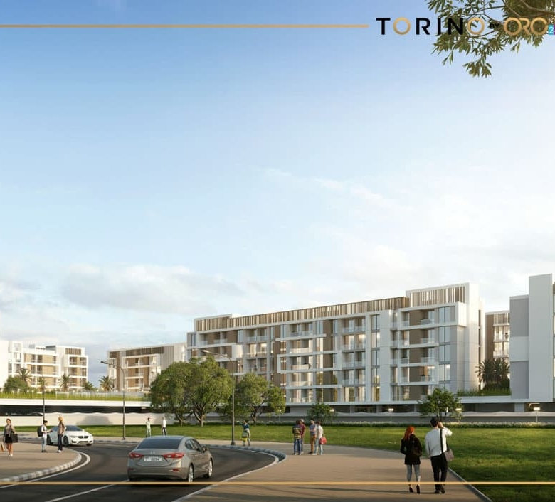 בנייני דירות מודרניים של ORO24, בעלי חזיתות לבנות, משתרעים לאורך רחוב מתעקל בטורינו, שבו מטיילים הולכים ומכוניות נוסעות. עצים ושמיים בהירים משלימים את התמונה העירונית והעכשווית.