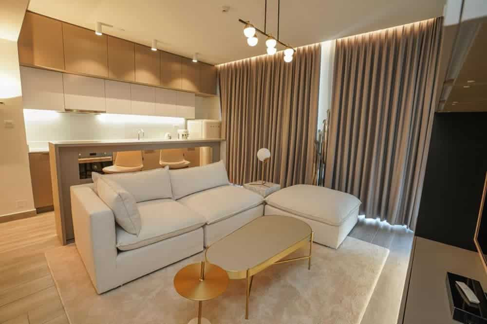 סלון מודרני בפרויקט “Noor Midtown” של חברת Deyaar, הכולל ספה מודולרית לבנה, שולחן קפה מוזהב ושולחן צד תואם. וילונות מהרצפה עד התקרה מכסים את החלונות הגדולים, וניתן להבחין במטבח פתוח ובכסאות בר. גוונים חמים ונייטרליים בכל החלל. סלון מודרני בפרויקט "Noor Midtown" של חברת Deyaar, הכולל ספה מודולרית לבנה, שולחן קפה מוזהב ושולחן צד תואם. וילונות מהרצפה עד התקרה מכסים את החלונות הגדולים, וניתן להבחין במטבח פתוח ובכסאות בר. גוונים חמים ונייטרליים בכל החלל.