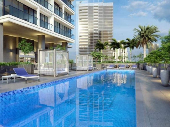 הבריכה החיצונית המודרנית ב-Catch Residences מוקפת בכיסאות נוח, בקתות נופש ועציצים, כשברקע ניצב מגדל רב-קומות ועצי דקל תחת שמיים מעוננים חלקית.